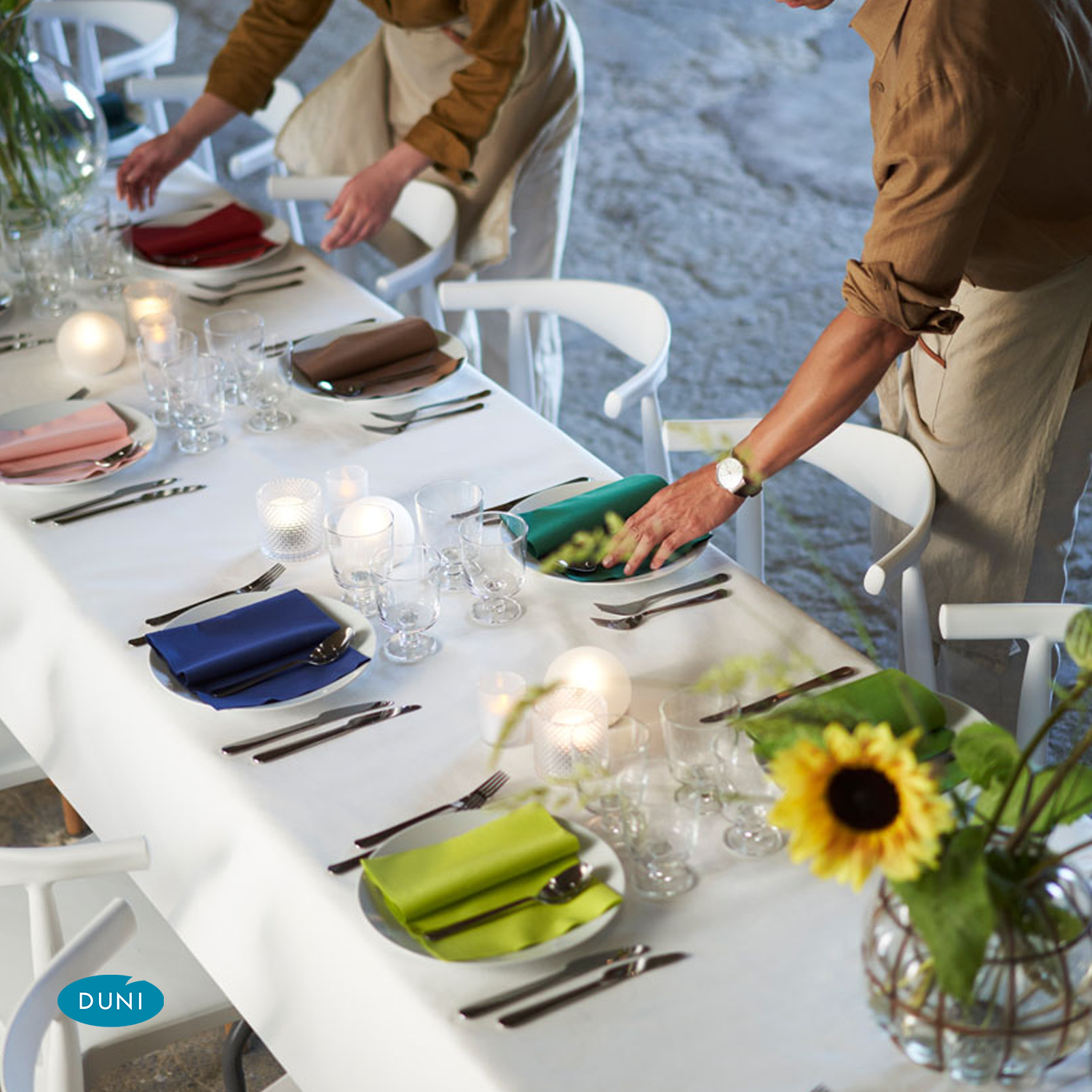Ein gedeckter Tisch mit einer weißen Tischdecke, jeder Teller hat eine anders farbige Serviette