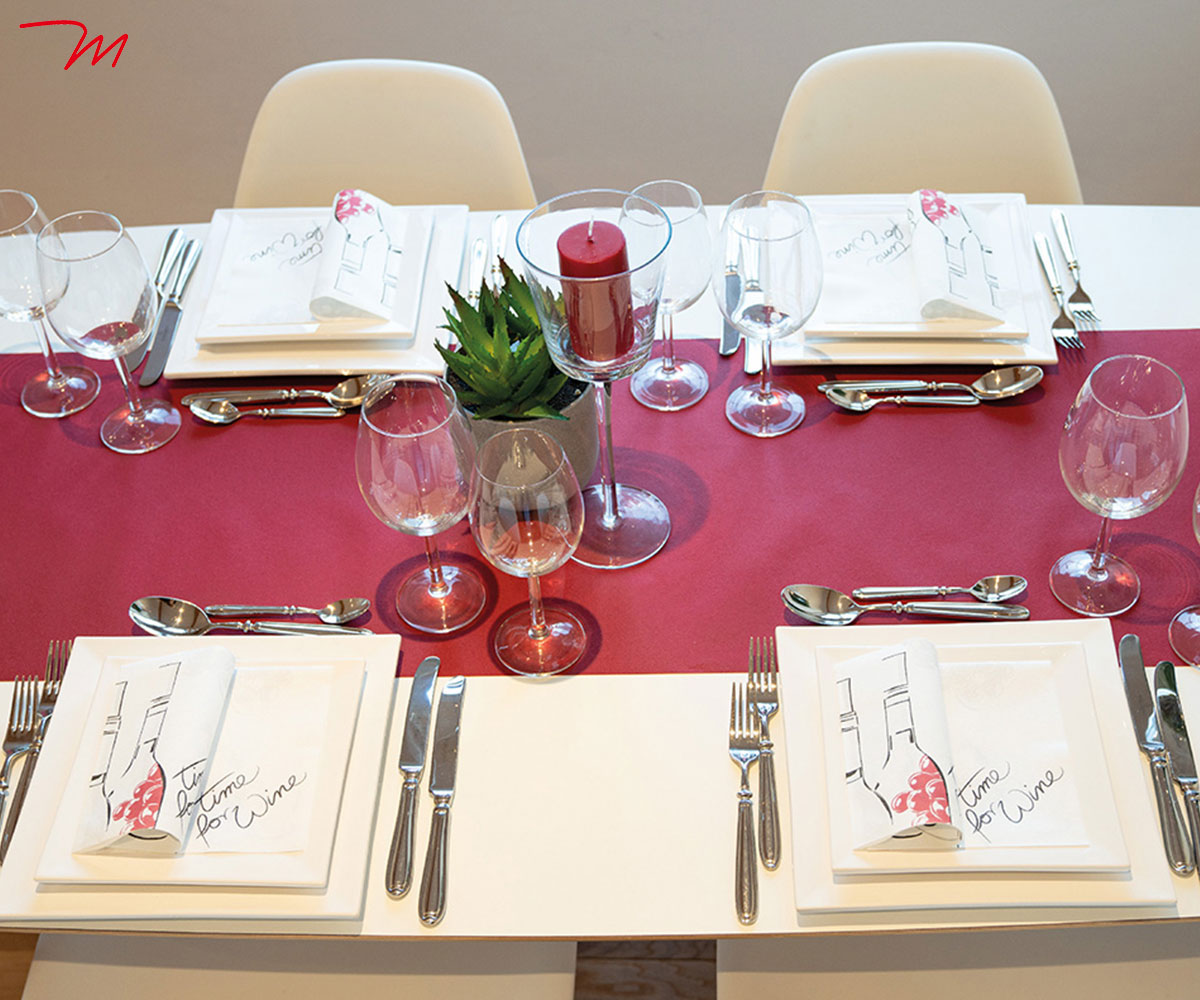 Elegant gedeckter Tisch mit farblich abgestimmten Servietten und Tischläufer, dekoriert im Wein-Thema mit Gläsern und Traubendetails