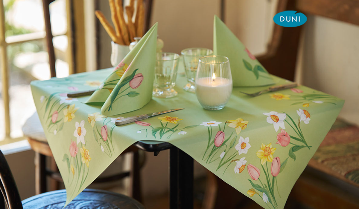 Ein kleiner gedeckter Tisch mit hellgrüner Tischdecke und Servietten mit Frühlingsblumen