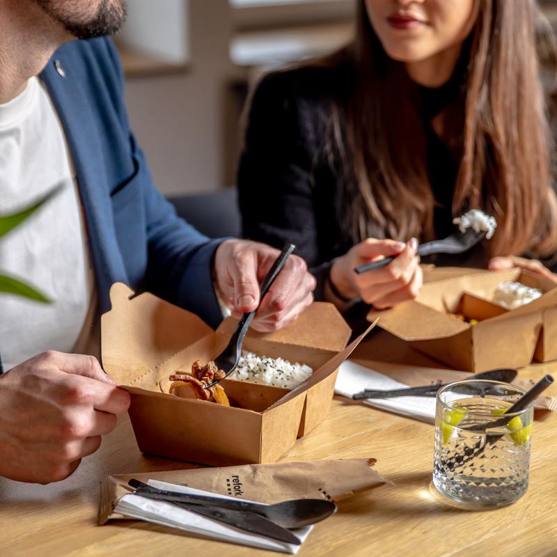 Schwarzes Besteck auf einem Tisch mit Essen und Personen beim Essen