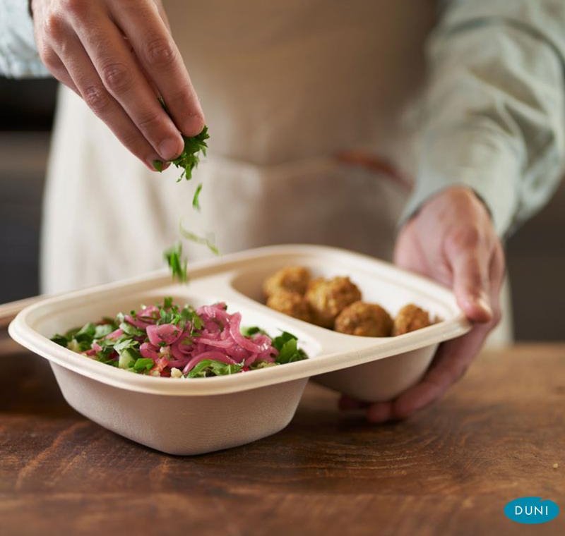 Eine Menüschale, gefüllt mit Essen, die von einer Person gehalten wird, die das Essen würzt